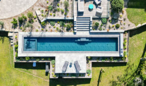 Dans le Morbihan, Piscine miroir longue et étroite réalisée par Passion Piscine, intégrée dans un jardin moderne signé Ropert Paysages
