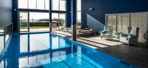 Réalisation de Piscine intérieure moderne en Bretagne, fauteuils de charme et transats confortables sur les abords